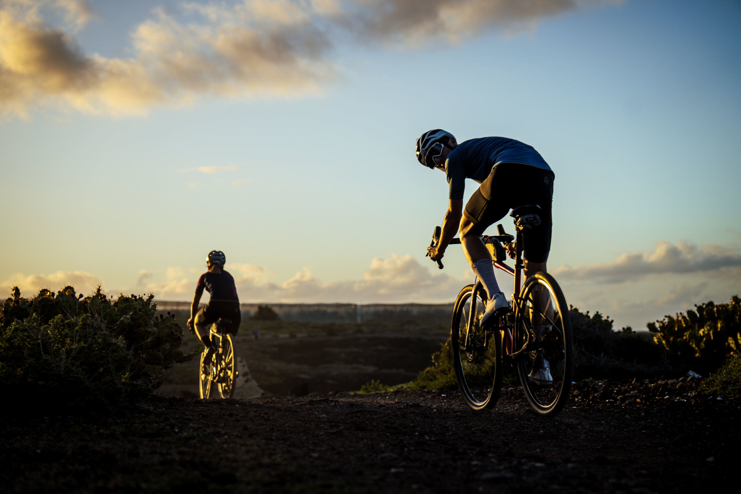 Two cyclists ride into the golden sunset on a rugged trail
