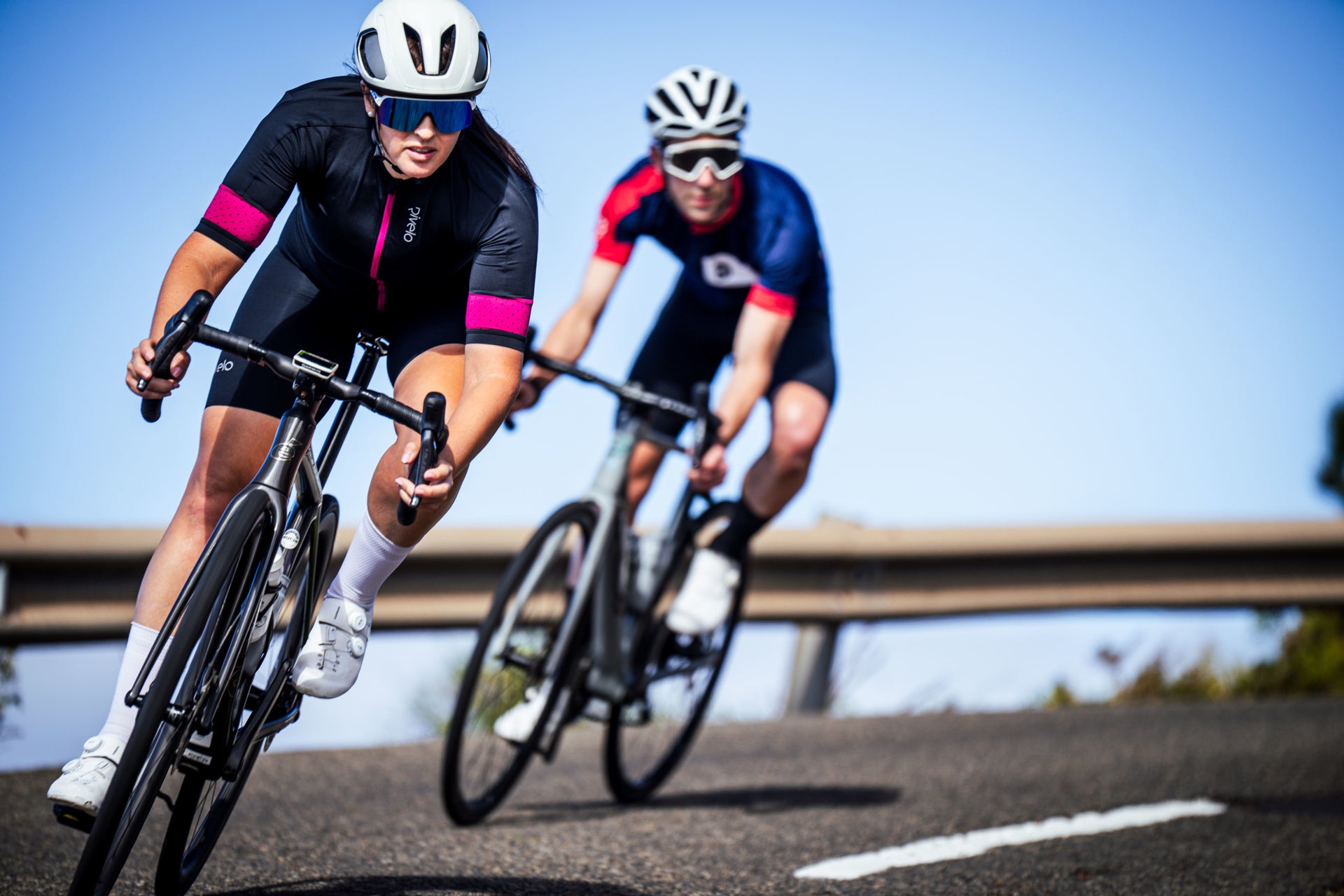Two cyclists cornering at speed on a sunlit road
