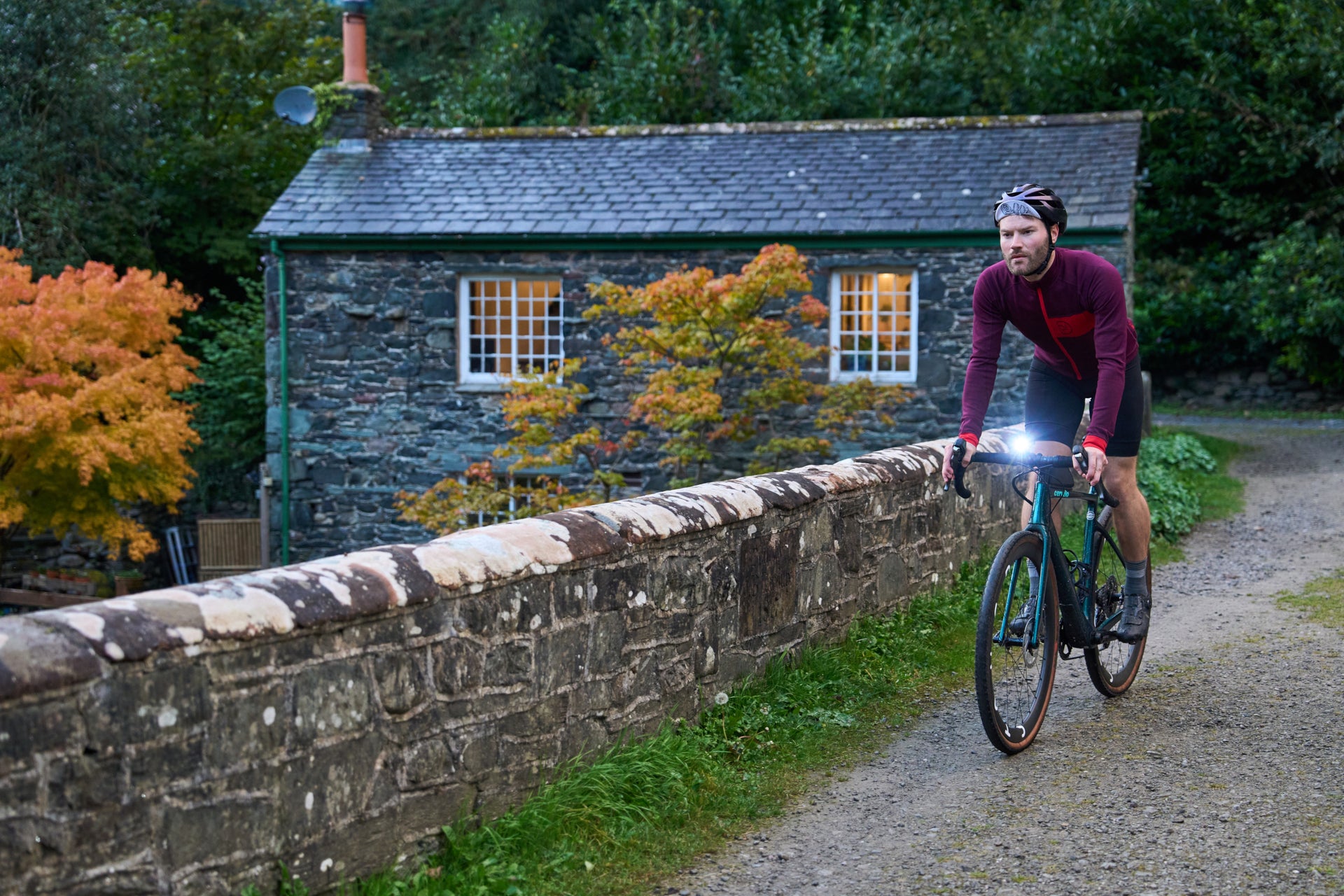 Cyclist riding across a stone bridge past a cottage in autumn