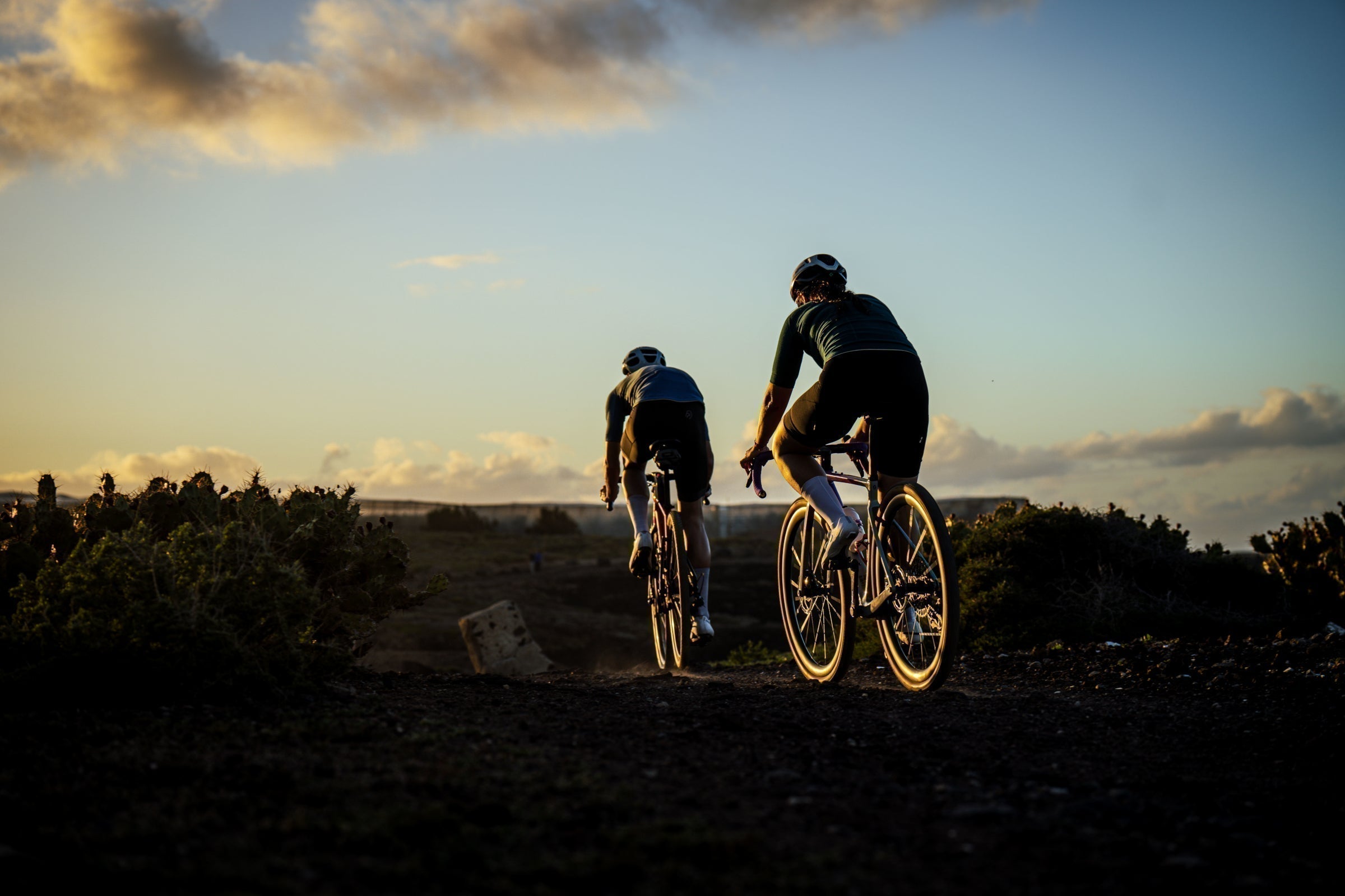 Two cyclists riding into the sunset on a gravel trail
