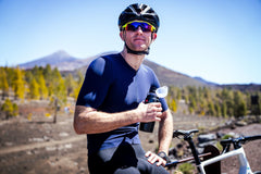 A man in cycling kit resting with a water bottle in a mountain landscape