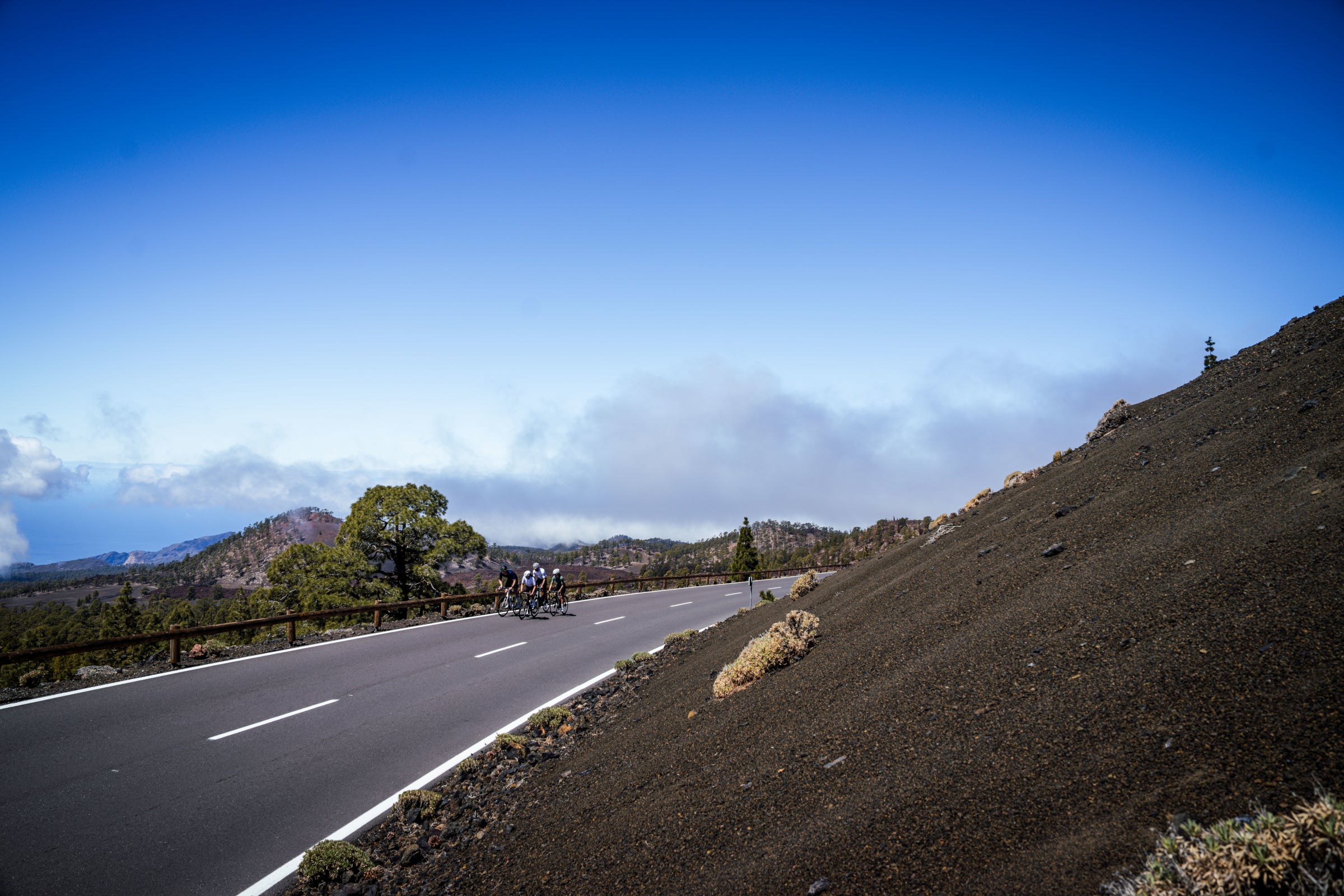 Cyclists riding on a winding mountain road under a clear blue sky