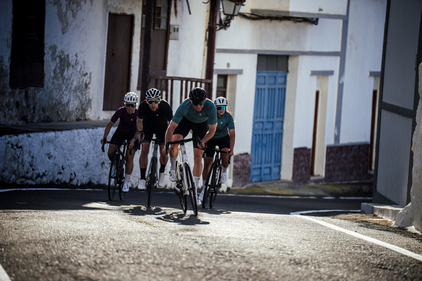 Four cyclists riding close together through a rustic village street