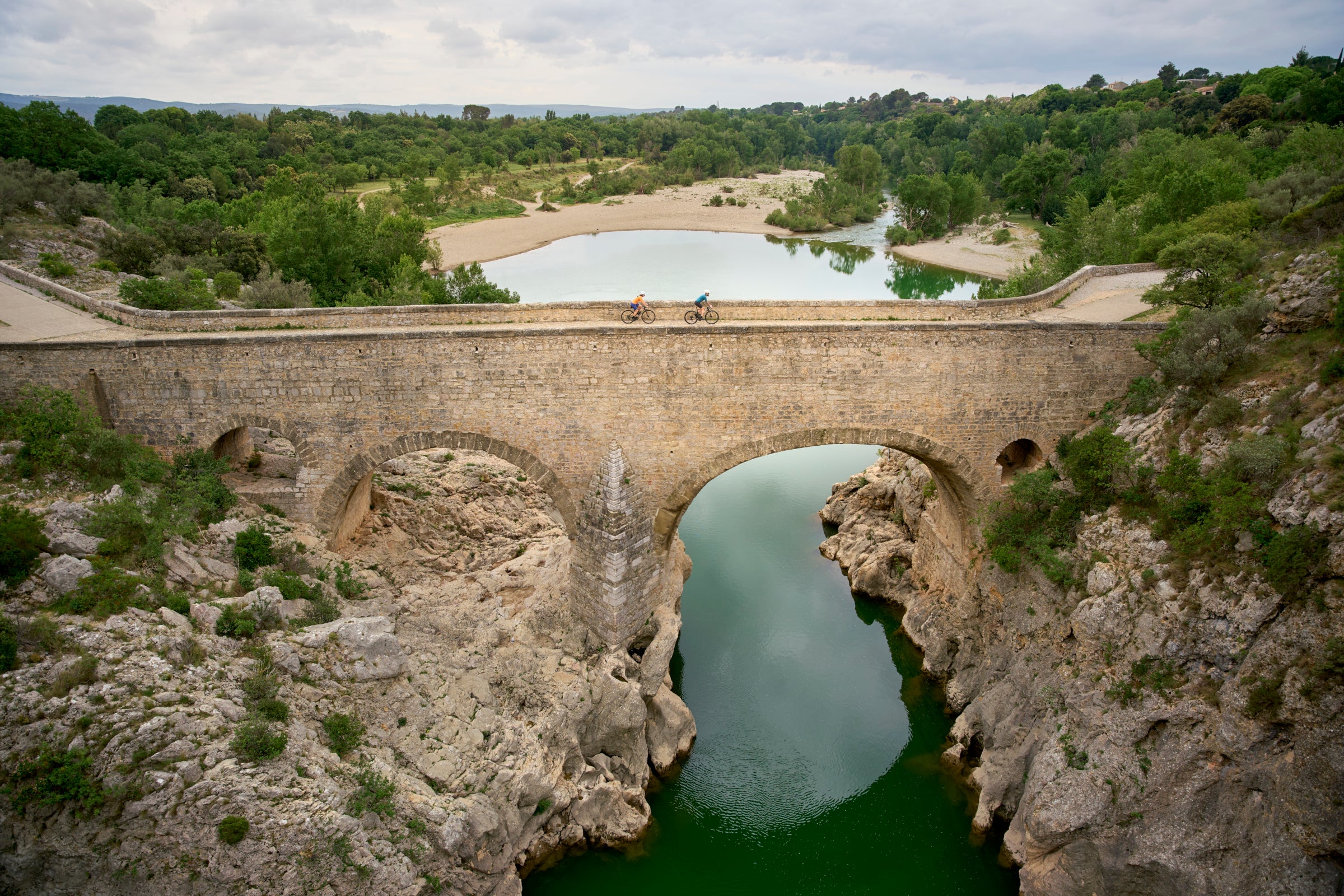 Two cyclists crossing a stone bridge over a river