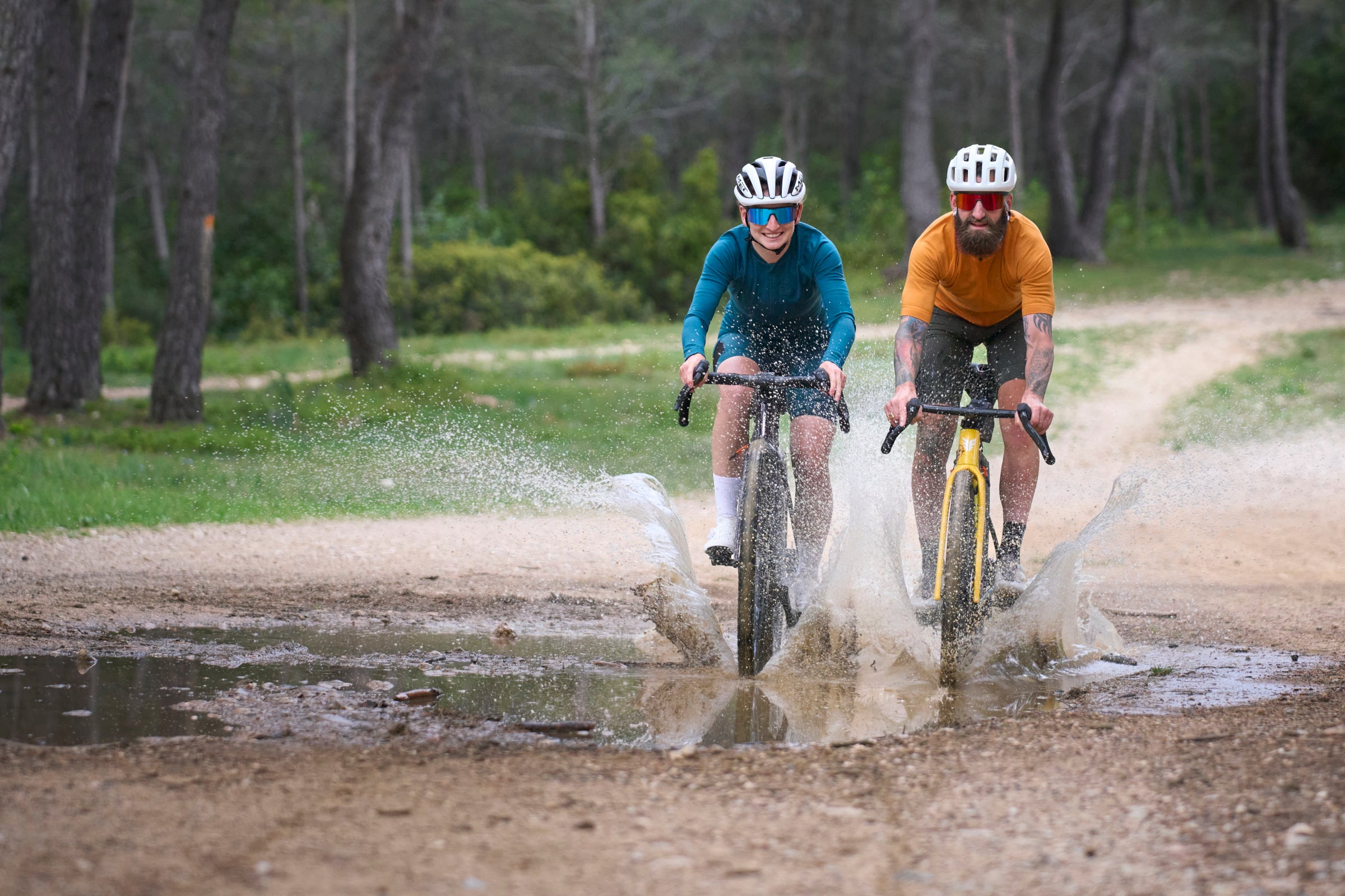 Two cyclists riding gravel bikes through a muddy puddle