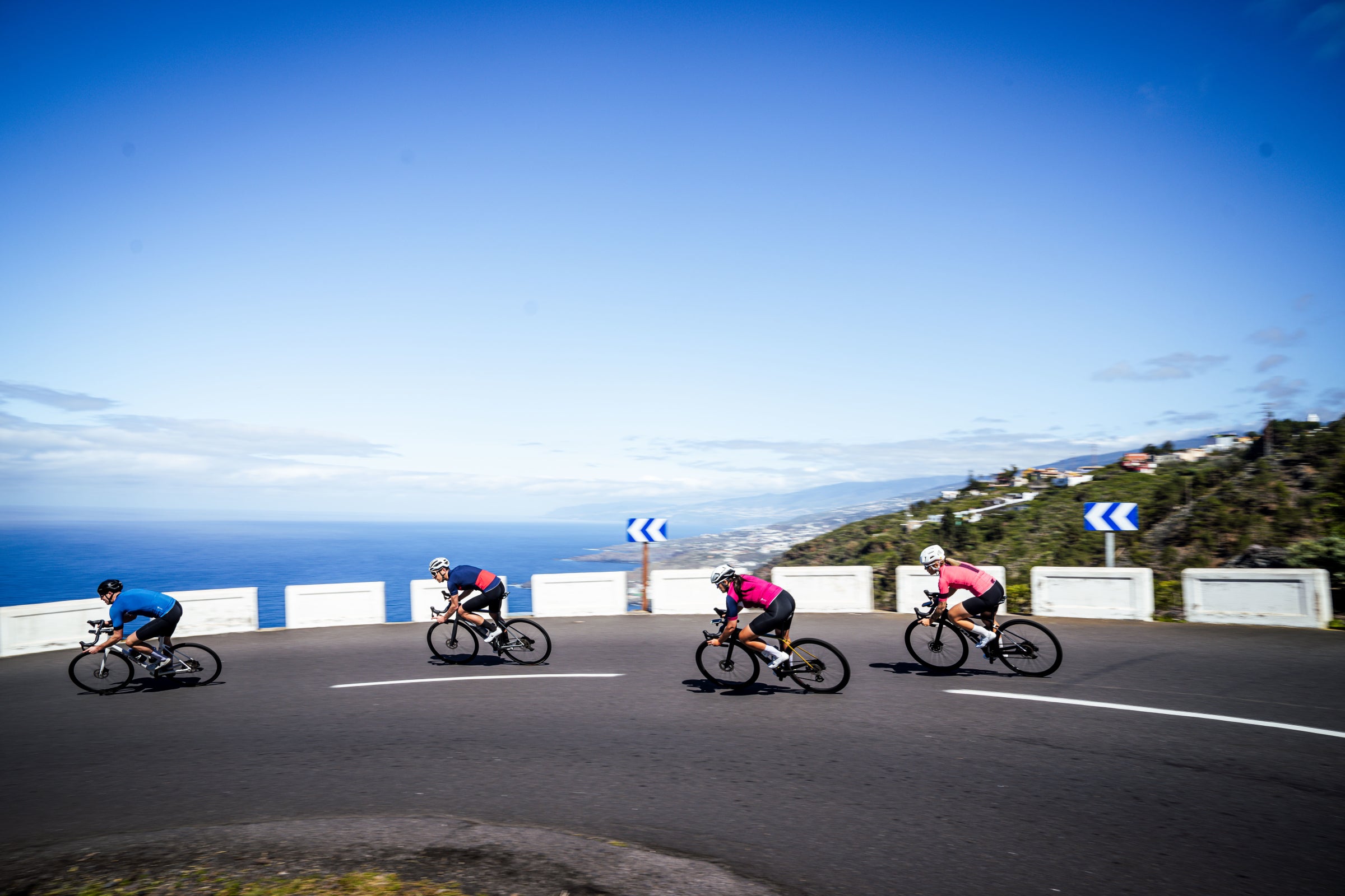 Four cyclists speeding downhill on a coastal mountain road
