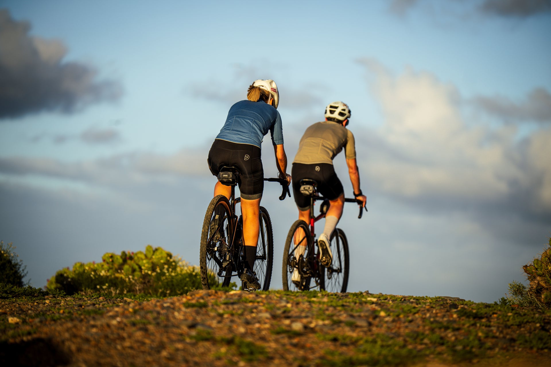 Two cyclists climbing a gravel trail under a wide open sky