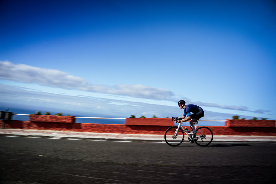 Cyclist in aero position riding along a coastal road under a bright blue sky