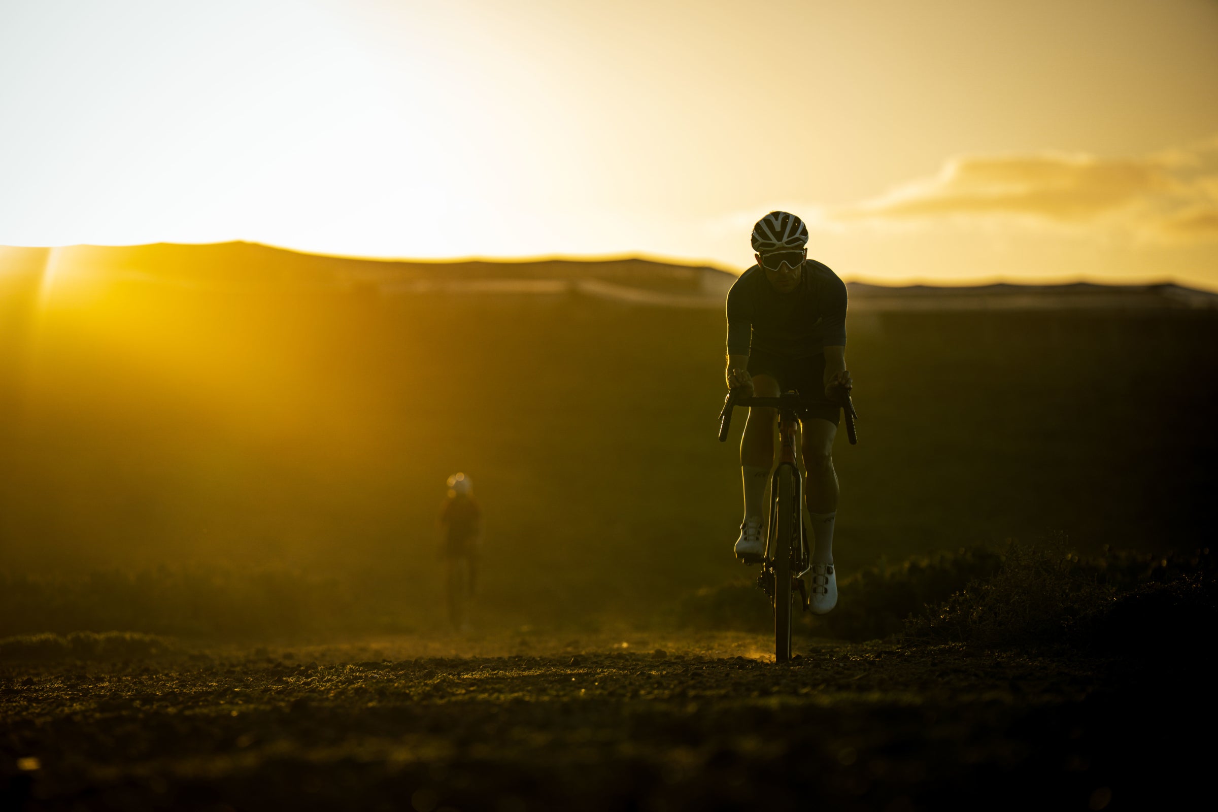 Two people on bicycles in a desert landscape with a golden sunset